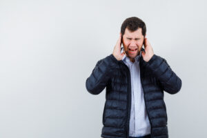 The young man is closing his ears with hands on white background